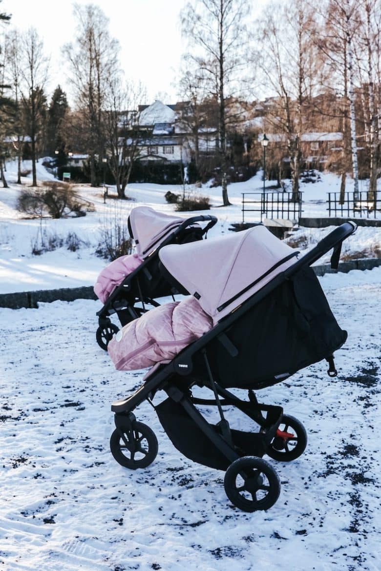 two baby strollers in the snow in front of a house